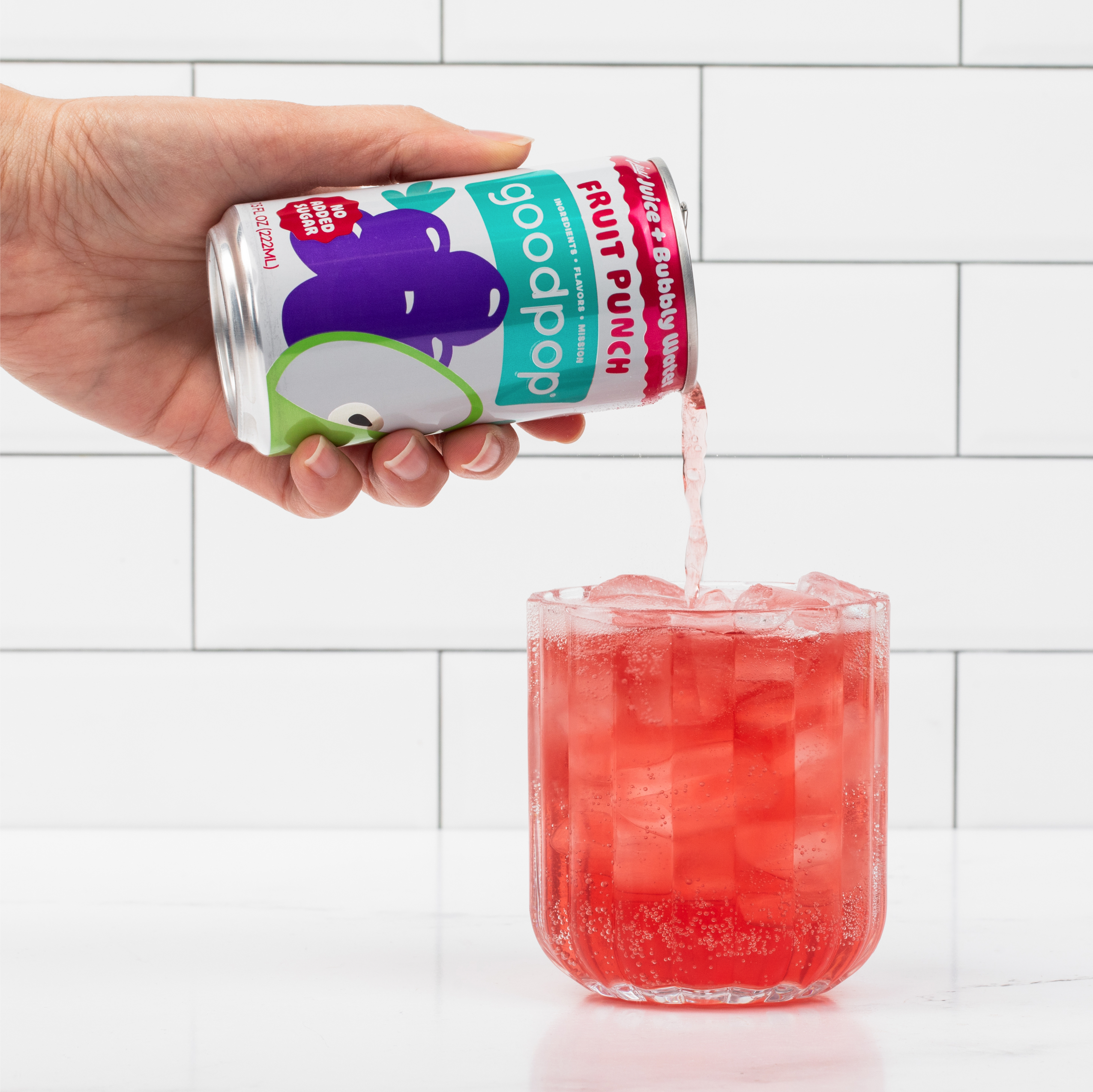 Woman pours GoodPop Fruit Punch Mini Can into a glass that sits on marble kitchen counter