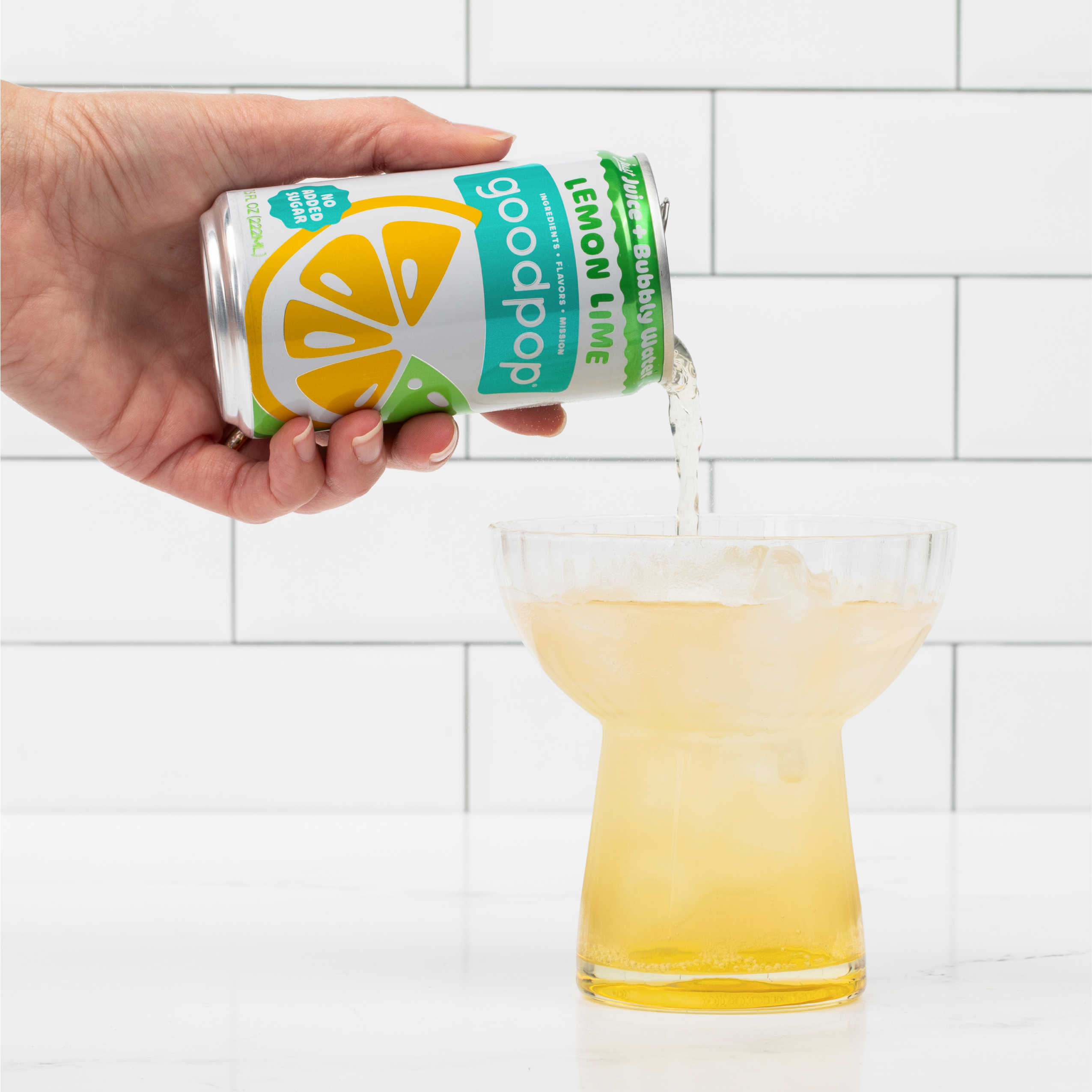 Woman pours GoodPop Lemon Lime Mini Can into a fluted glass that sits on marble kitchen counter