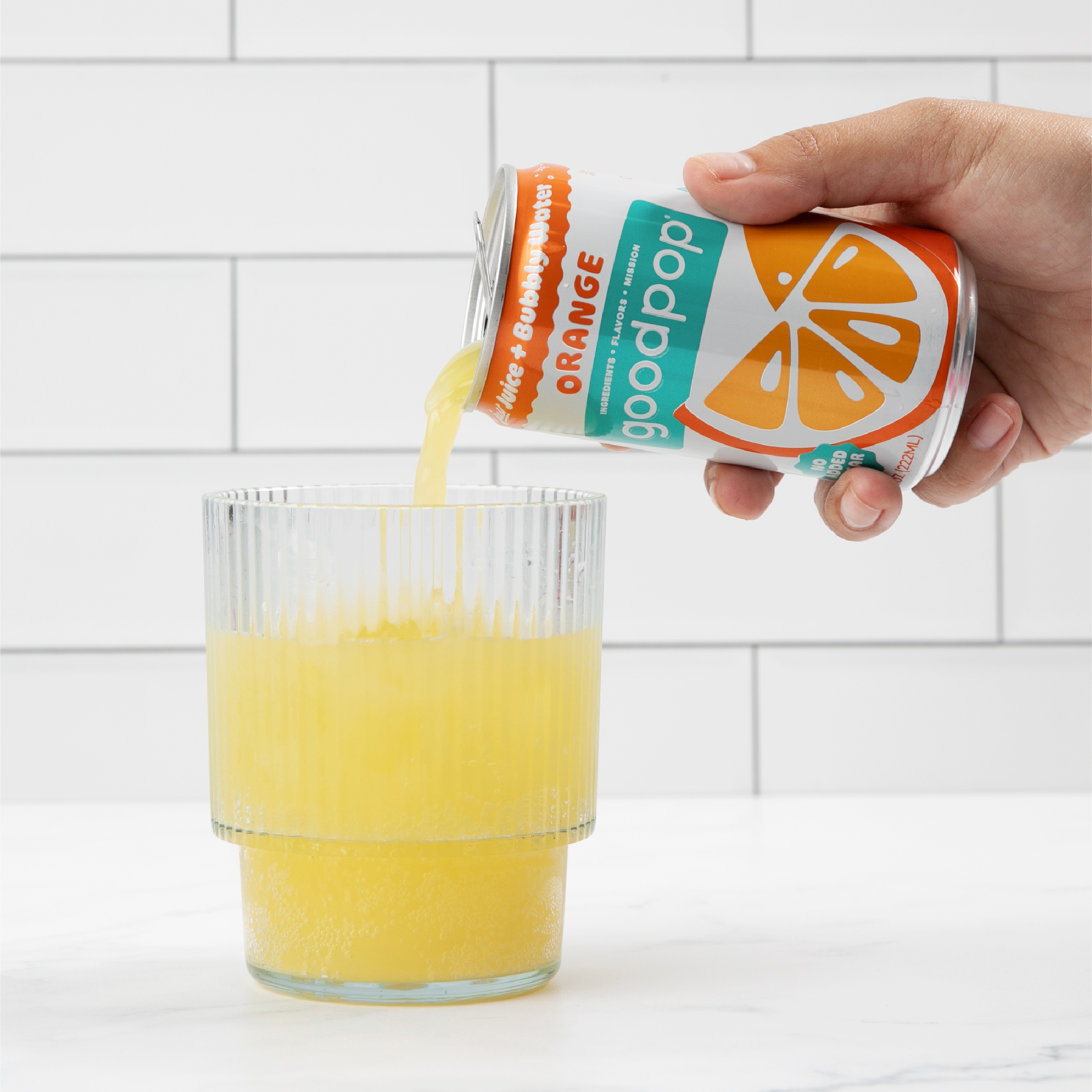 Woman pours GoodPop Orange Mini Can into a fluted glass that sits on marble kitchen counter