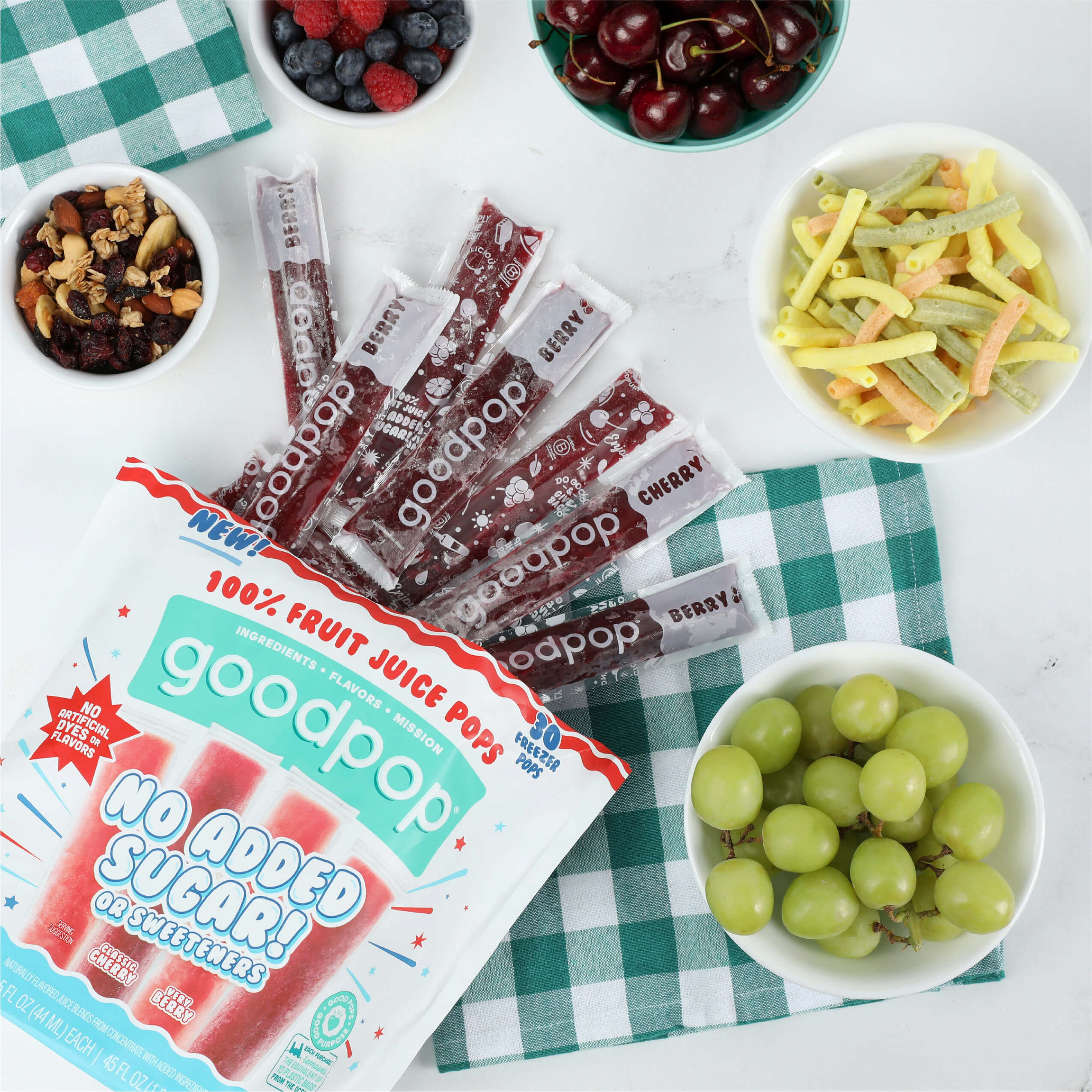 Opened bag of GoodPop Cherry Berry Freezer Pops lay on a picnic table with other healthy snacks