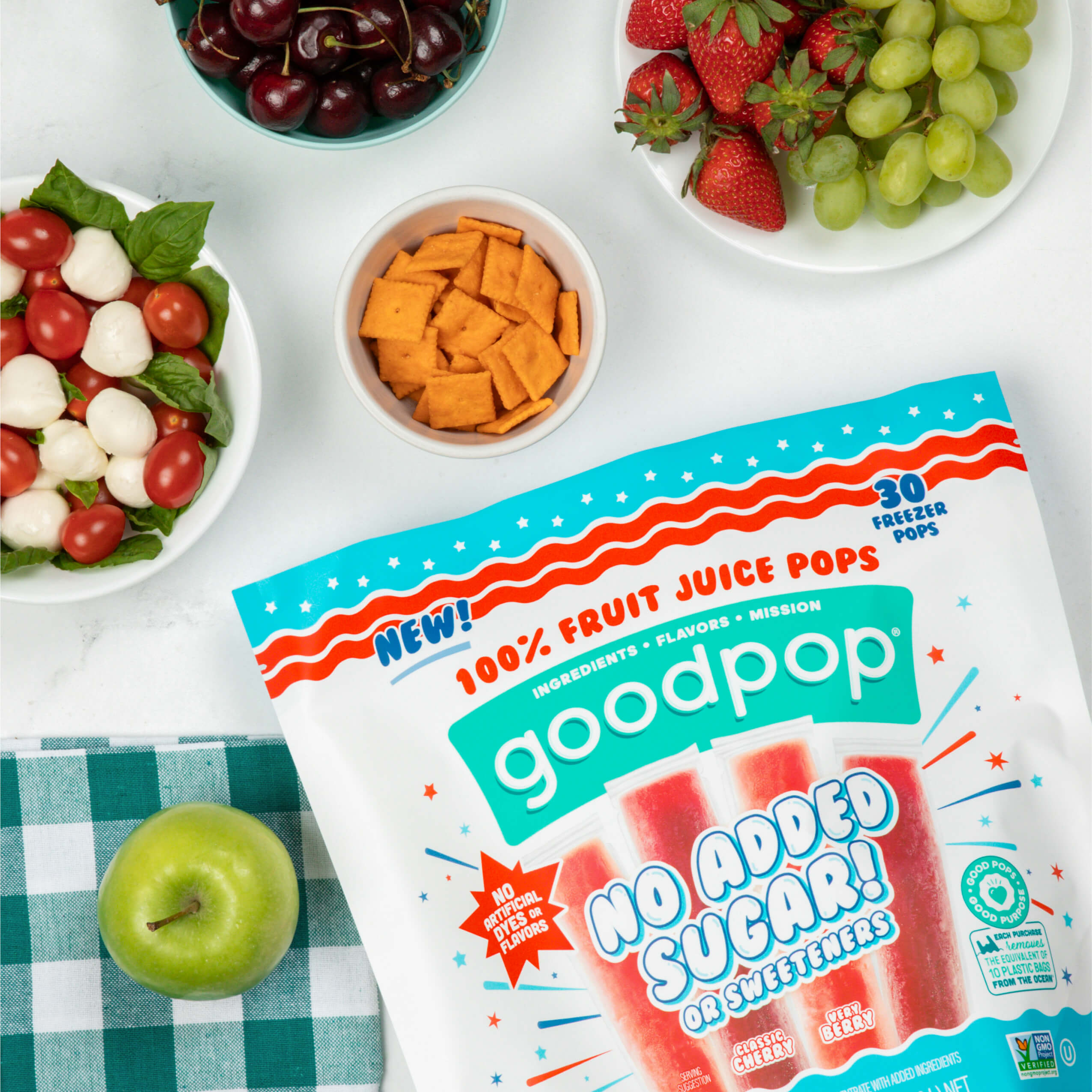 Close bag of GoodPop Cherry Berry Freezer Pops lay on a picnic table with other healthy snacks