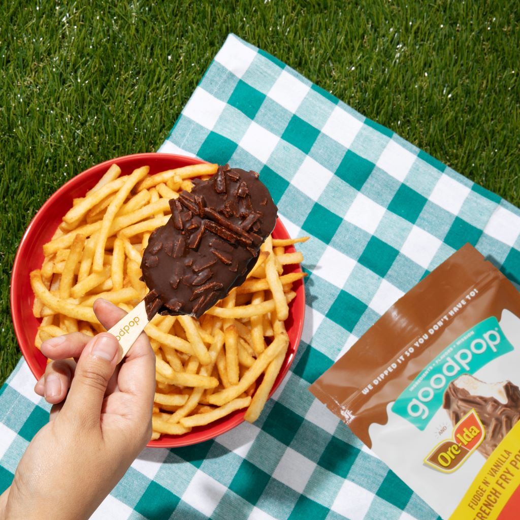 Hand holds Fudge n' Vanilla French Fry Pop above a bowl of french fries at a picnic